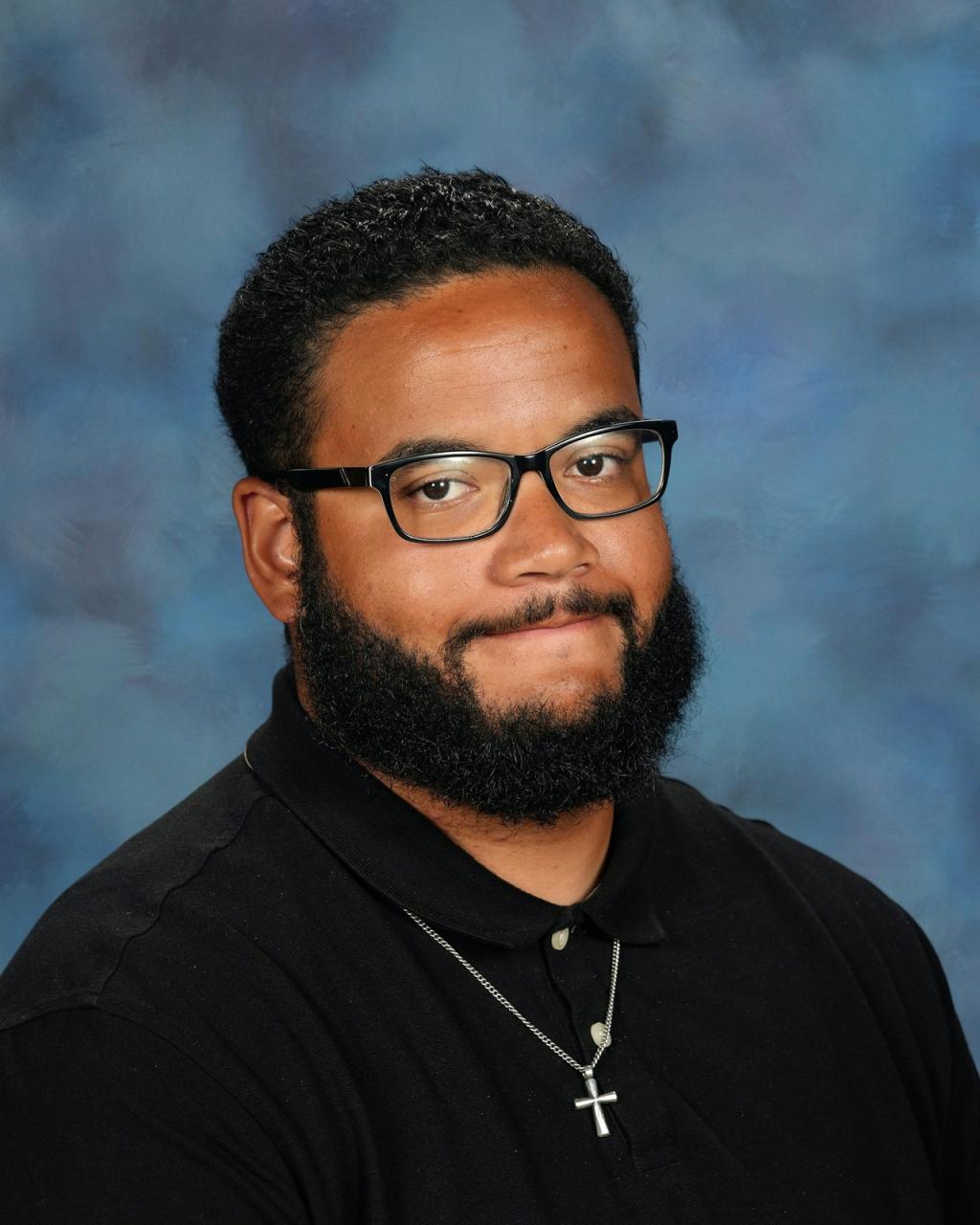 A man with dark hair, facial hair and black glasses